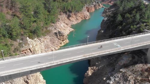 Person is riding on road bicycle on empty bridge over mountain water reservoir