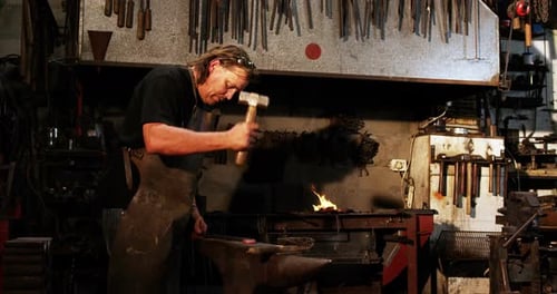 Blacksmith Hammering Metal in Dark Workshop