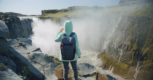 Frau steht am Stony Cliff Edge und genießt den beeindruckenden Detifoss-Wasserfall in Island
