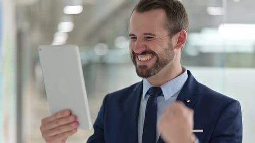 Man Celebrates Success Using Tablet in Office