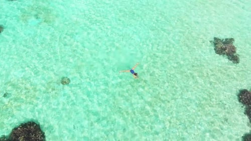 Aerial slow motion: woman snorkeling on coral reef tropical sea from above
