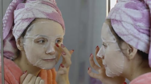 Woman Applying Cosmetic Face Mask in Bathroom. Skincare Spa. Facial Mask