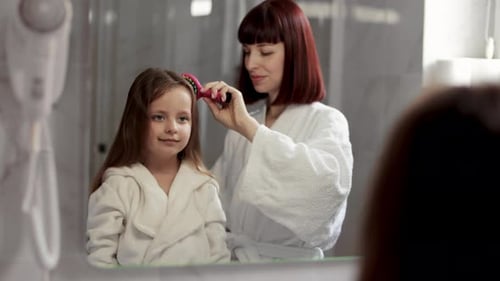 Mother brushing child's hair in bathroom mirror