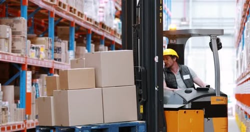 Male warehouse worker using forklift truck for lifting stock