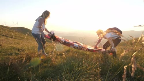 Couple Spreading Blanket on Beautiful Hillside at Sunset