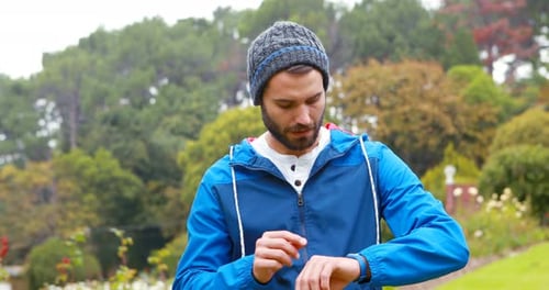 Man Checks Watch and Earbuds in a Park