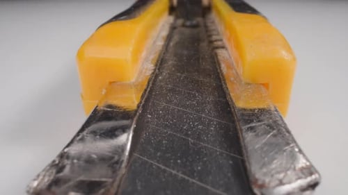 Motion Along Box Cutter with Open Blade on White Table