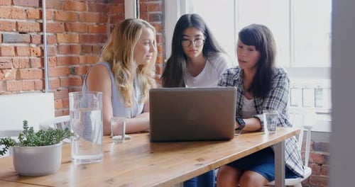 Three Young Adults Collaborate on Laptop in Office