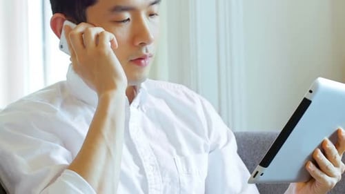 Man Using Tablet While Talking on Phone Indoors