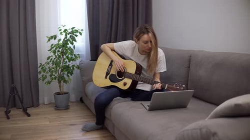 Woman Plays Acoustic Guitar at Home with Laptop