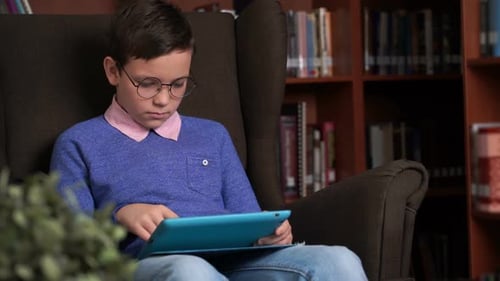 Cute Schoolboy Uses the App on His Smartphone While Sitting in a Chair