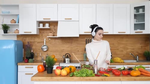 Young Woman Cooking Salad in Kitchen with Headphones
