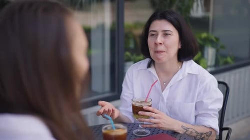 Positive Happy Woman Talking with Friend Gesturing in Slow Motion Sitting at Table in Sidewalk Cafe