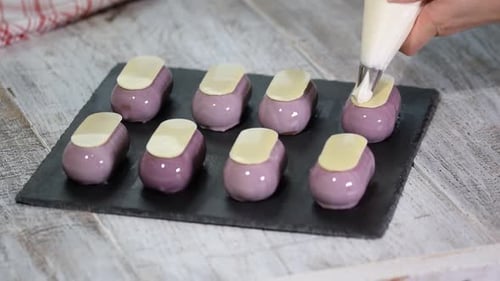 Chef Decorates Small Purple Glazed Desserts with Cream