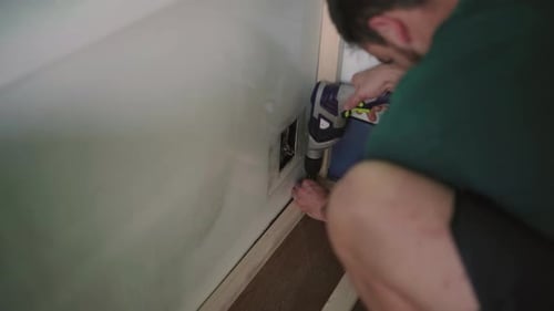 Close up shot of male person boring wood with electric drill inside own camper van for traveling.