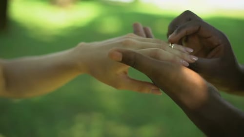 Gemischtrassige Ehe, männliche Hand legt goldenen Ring auf den Finger der Braut, Hochzeitszeit