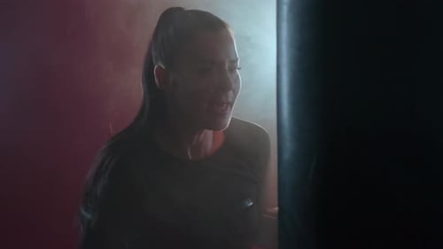 Slow motion aggressive athletic woman boxer in boxing gloves trains in a dark gym.