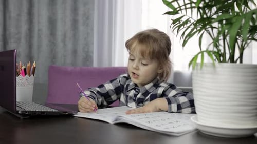 Child Writes at Desk During Online Lesson