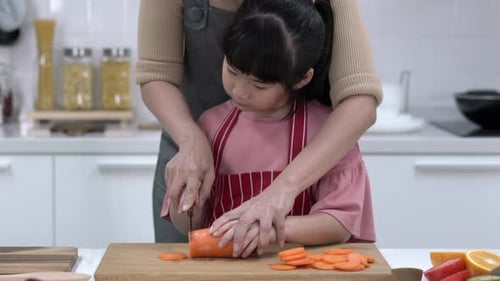 Girl learning to cut carrots in bright kitchen