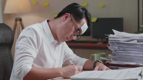 Close Up Of Sick Asian Man Writing Something On Paper While Working Hard With Documents At Office