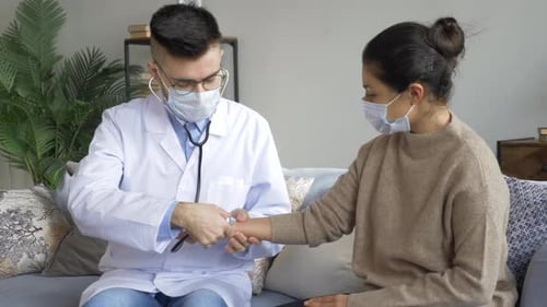 Doctor Checks Patient Pulse at Home Wearing Masks