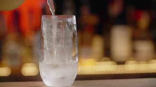 Limonade is Being Poured to the Ice Cube in Cocktail Glass on the Bar Counter in Slow Motion Full