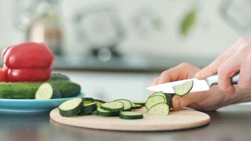 Hand with Knife Cuts Vegetables on a Wooden Cutting Board