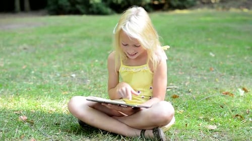 Little Lively Cute Girl Sits in the Park and Writes Messages on the Tablet