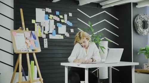 Attractive Business Woman Talking on the Cell Phone and Writing Down Something
