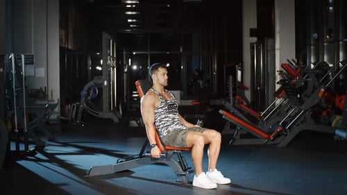 Attractive Male Bodybuilder Exercising Hands With Dumbbells on Bench Chest and Press Workout in Gym