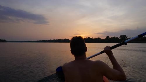 A Man Kayaks on a Calm River Towards the Sunset