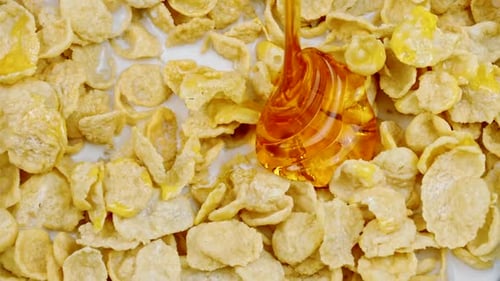 Honey Pours Onto Corn Flakes Cereal with Milk