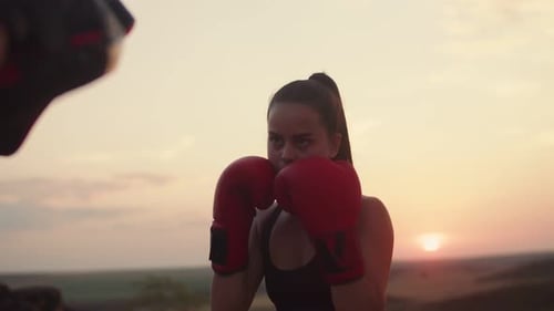 Confident Female Boxer in Black Suit Trains at Sunset in Field and Hits Her Paws for Boxing
