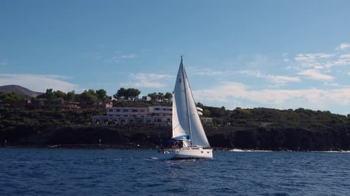 Moving Sailing Yacht Against Rocky Mountains with Huge Hotel Complex