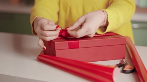 Woman Tying Ribbon on Red Gift Box