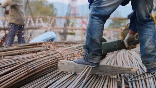 Close-up view of legs in foreground of a worker, cutting pipes with a saw blade.