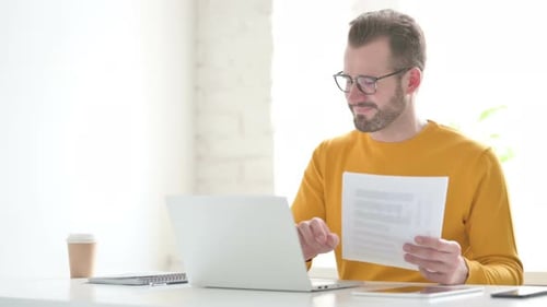 Bearded Man Working at Laptop with Papers