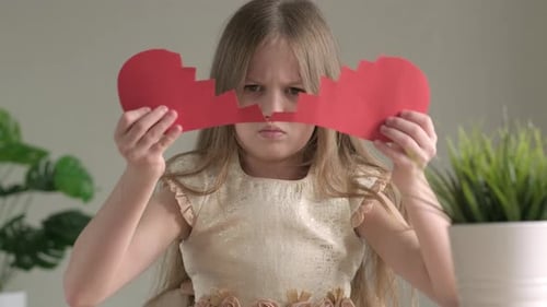 Upset Child Holding Two Pieces of a Red Paper Heart Heartbreak and Heartache Concept