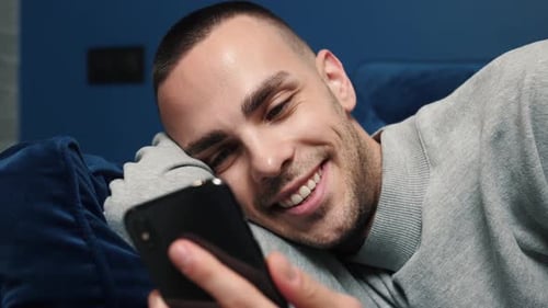 Man Smiling, Looking at Mobile Phone on Couch