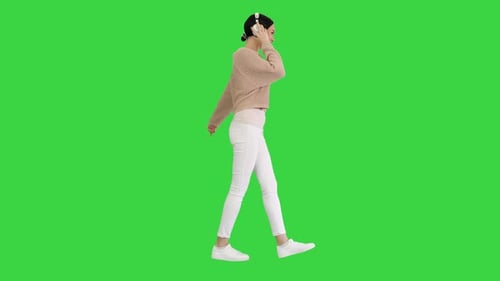 Smiling Female with Headphones Walking and Dancing To the Music on a Green Screen, Chroma Key.