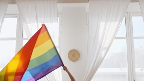 Person Waves Rainbow Pride Flag in Bright Room