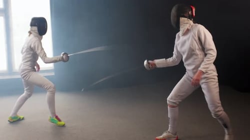 Two Young Women Having an Intense Training in a Fencing Duel in the Dark Smoky Studio