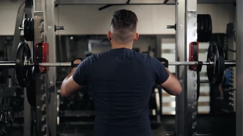 Hands of a Man in Front of the Barbell on the Background of His Back in the Black Pants