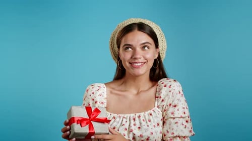 Cheerful Woman Holding Gift in Front of Blue Background