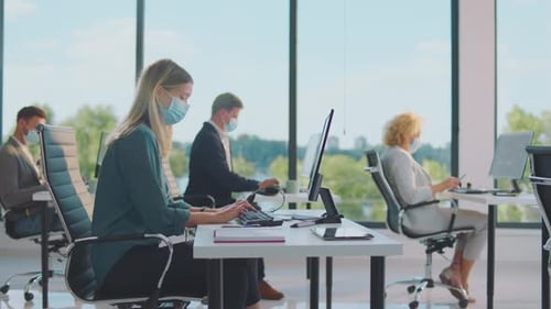 Workers Wearing Masks Typing At Computers In Modern Office