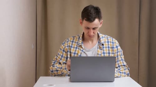 Young Man Angry Typing on Laptop at Table
