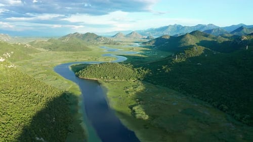 Bends and curves of blue river flowing through green valley toward distant mountains.