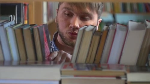 Young Man Browsing Through the Racks of Books in a Library