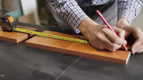 Woodworker Measuring Wood with Tape Measure and Pencil