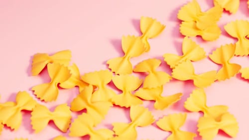 Vibrant Yellow Farfalle Pasta Shifting on Pink Background